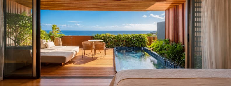 Private sea-view suite in La Réunion with outdoor hot tub, deck, and ocean-facing lounge chairs under wood-paneled shade.