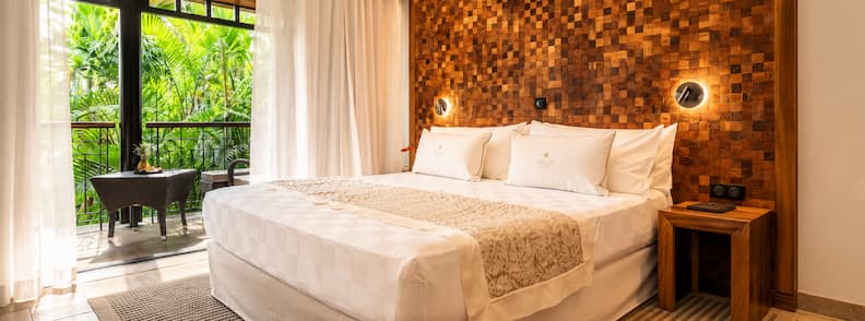 Elegant hotel room at Palm Hotel & Spa in La Réunion with wood accent wall, soft lighting, and a private balcony overlooking tropical gardens.