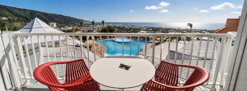 Balcony view from Hôtel Exsel Créolia overlooking Saint-Denis, with a pool in the foreground and the Indian Ocean in the distance.
