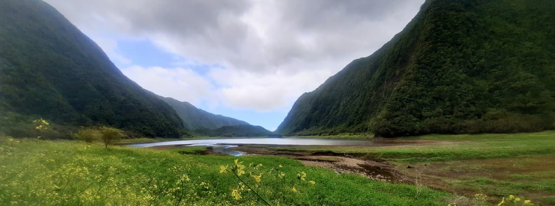 beginner hikes la reunion grand etang easy trails Grand Étang in La Réunion surrounded by steep green mountains, calm water, and an easy hiking trail through the highlands.