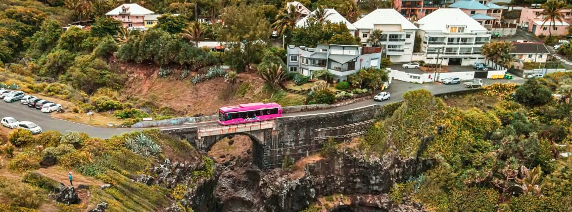 car jaune reunion public transport reunion island Car Jaune bus crossing a bridge in La Réunion with residential neighborhoods and volcanic landscapes surrounding the regional road network.