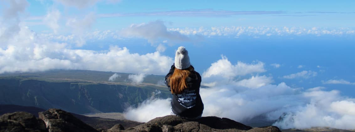 is la reunion worth visiting honest answer reunion island Traveler sitting above the clouds on a volcanic viewpoint in La Réunion overlooking mountains and the Indian Ocean.