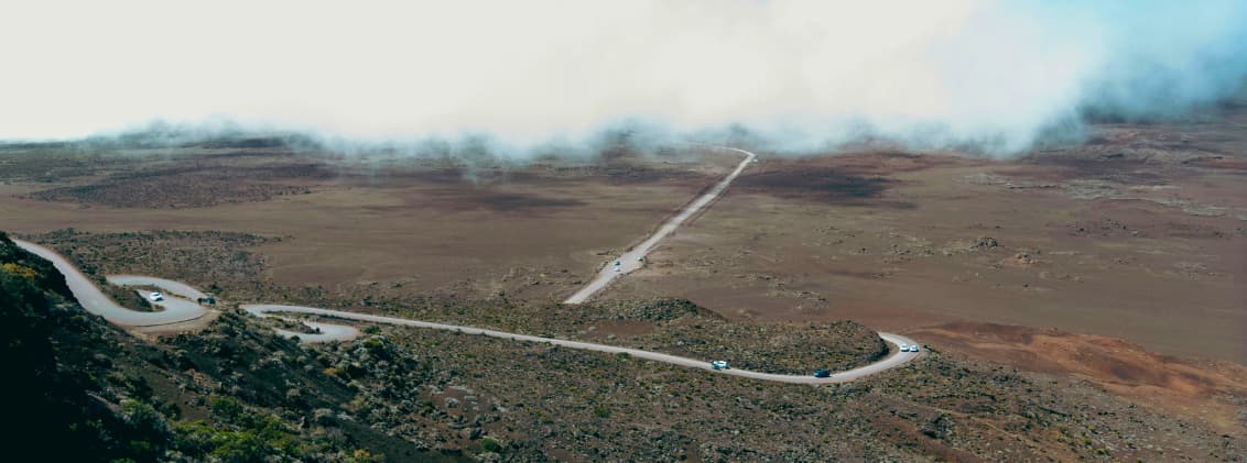 la reunion driving tips route du volcan road trip Cars driving along the Route du Volcan in La Réunion, with fog rolling over the volcanic plains and winding mountain roads.