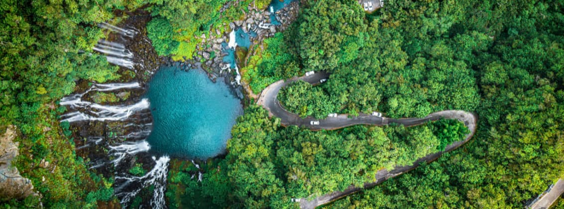 la reunion travel guide indian ocean island waterfalls road trip Aerial view of La Réunion waterfalls, turquoise river pools, dense forest, and a winding road through the Indian Ocean island’s volcanic landscape.