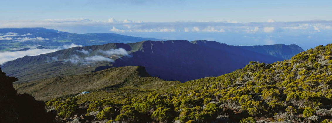 La Reunion Travel Guide. Panoramic view from the Piton des Neiges trail in La Réunion, with volcanic ridges, highland vegetation, and clouds drifting above the cirques of Réunion Island.