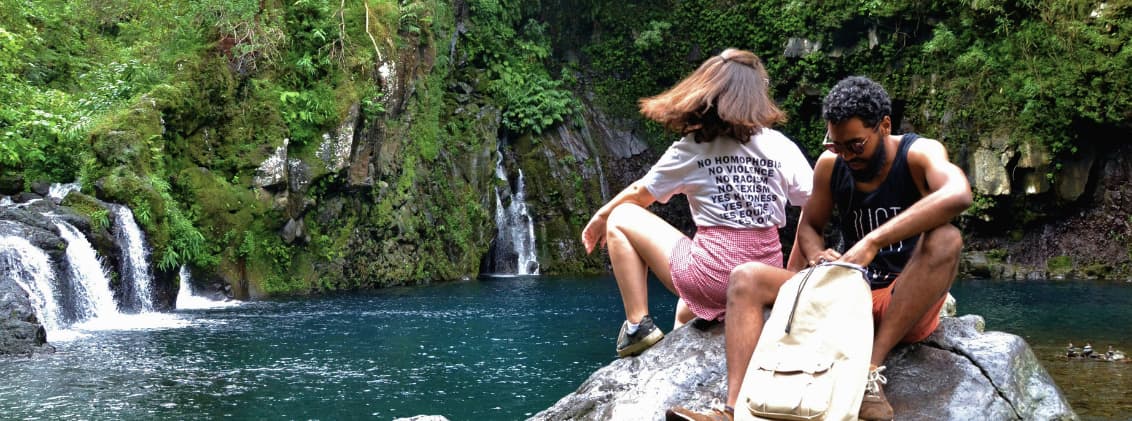 la reunion waterfalls nature stops east coast reunion Travelers relaxing beside a waterfall pool in La Réunion surrounded by lush tropical vegetation and volcanic rock formations.