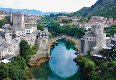 Historic stone bridge over the river in Mostar Bosnia and Herzegovina surrounded by mountains and old town buildings.