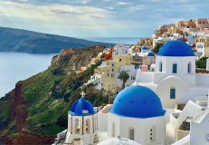 Blue-domed churches and white cliffside buildings overlooking the sea in Santorini Greece.