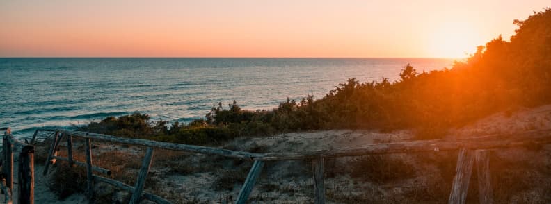 Wooden fencing and dune vegetation at sunset above a free beach in Sperlonga, with the Tyrrhenian Sea stretching across the horizon.