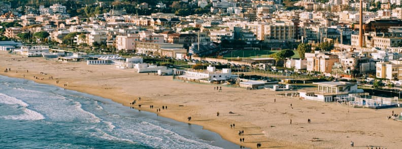 Aerial view of Serapo beach in Gaeta with a wide sandy shoreline, gentle Tyrrhenian waves, beachfront lidos, and the coastal town behind it.