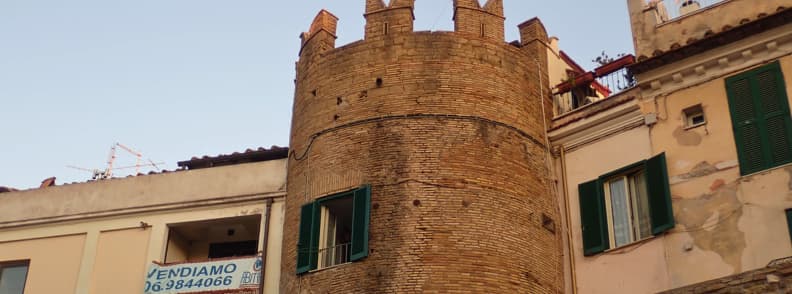 Nettuno Medieval Tower Home in Borgo Medievale Medieval brick tower built into residential homes in Nettuno old town, with crenellations, green shutters, and private windows.