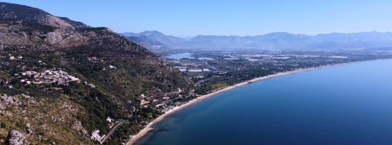 Aerial view of Terracina beach with a long sandy shoreline, deep blue Tyrrhenian Sea, rugged mountains, and the coastal plain of southern Lazio.