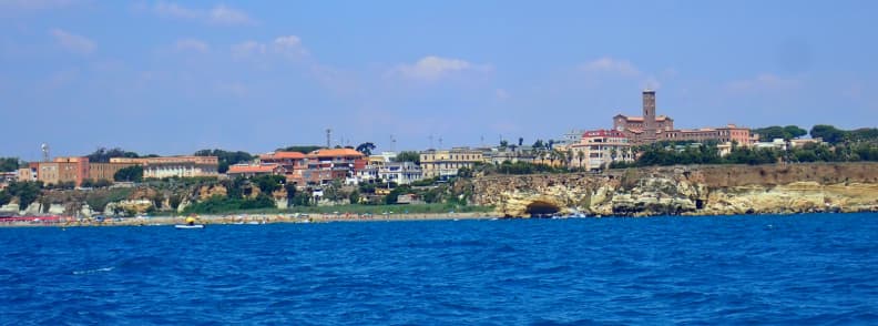 Sailing from Porto Romano to Nettuno on Lazio Coast Lazio coastline seen from a sailboat during the route from Porto Romano to Nettuno, with rocky cliffs, waterfront buildings, and the blue Tyrrhenian Sea.