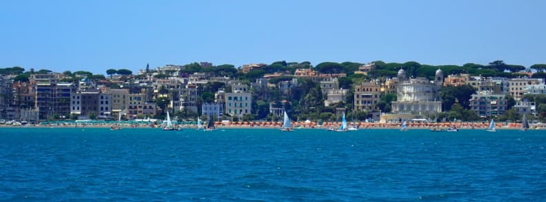 visit Anzio Italy Coastline and Beach Seen from the Sea Anzio, Italy, seen from the Tyrrhenian Sea, with waterfront buildings, sandy beaches, sailboats, and green hills along the Lazio coast.