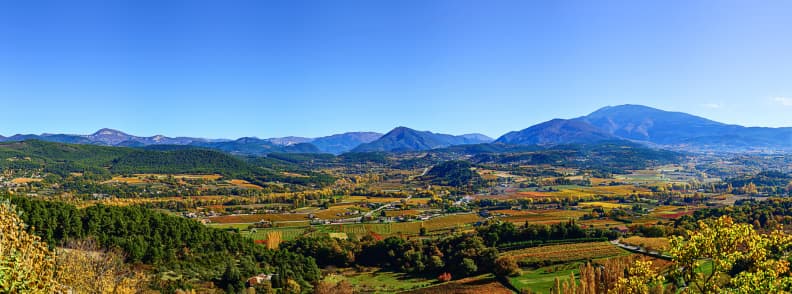 Best Time to Visit Provence in Autumn Valley Views Panoramic Provence valley in autumn with vineyards, patchwork farmland, wooded hills, and mountains beneath a clear blue sky.