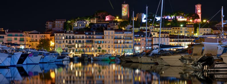 Cannes Old Port at Night on the French Riviera Yachts moored in the Old Port of Cannes at night with illuminated buildings and Le Suquet rising behind the marina