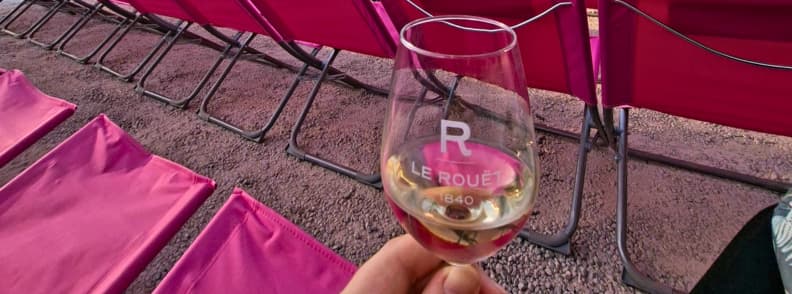 Glass of Château du Rouët white wine held beside pink chiliennes before a Les Musicales dans les Vignes concert in Le Muy.