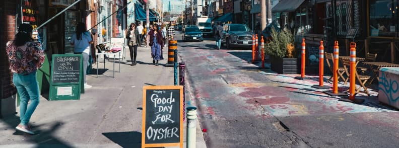 Kensington Market Toronto Two Day Couples Itinerary Pedestrians walking past restaurants and colourful storefronts in Kensington Market during two days in Toronto.