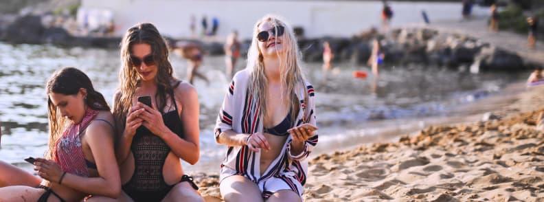 Mediterranean eSIM Coverage for Coastal Destinations Travelers using smartphones on a Mediterranean beach while relying on mobile data across Mediterranean destinations.