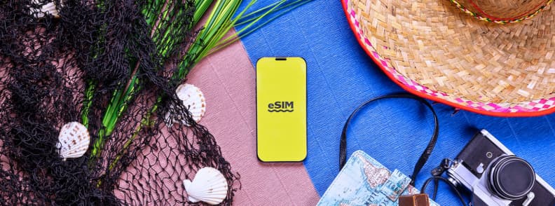 Mediterranean eSIM for Multiple Countries Travel Setup. Smartphone displaying an eSIM beside a straw hat, camera, map, and travel accessories for a Mediterranean Europe trip.