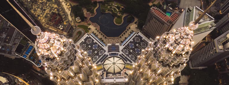 Top-down aerial view of the illuminated Petronas Twin Towers and surrounding KLCC buildings at night in Kuala Lumpur.