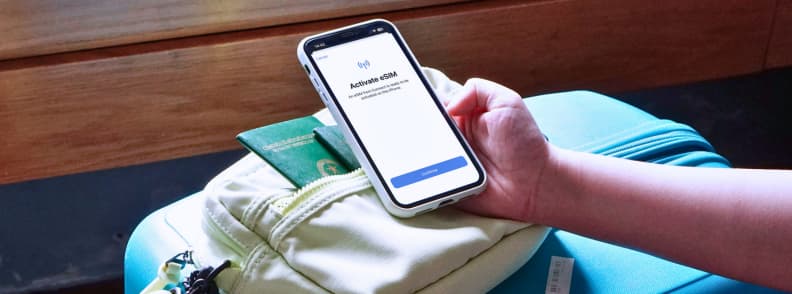 Set Up eSIM Before Flying to Europe Traveler activating an eSIM before flying to Europe on a smartphone beside a passport and packed luggage.