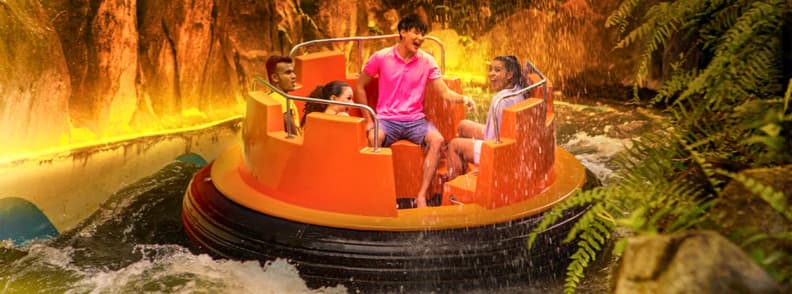 Family riding an orange circular raft through a jungle-themed river rapids attraction at Sunway Lagoon near Kuala Lumpur.