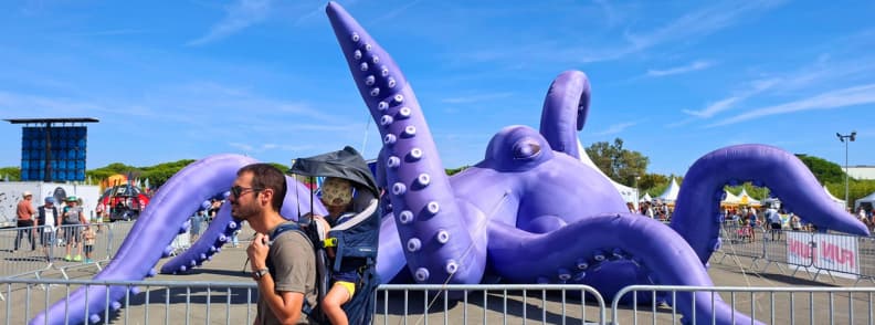 Frejus Air Festival Giant Purple Octopus Family Visit My husband carrying our 2-year-old son in a hiking carrier beside a giant purple octopus installation at the Fréjus International Air Festival at Base Nature François Léotard.