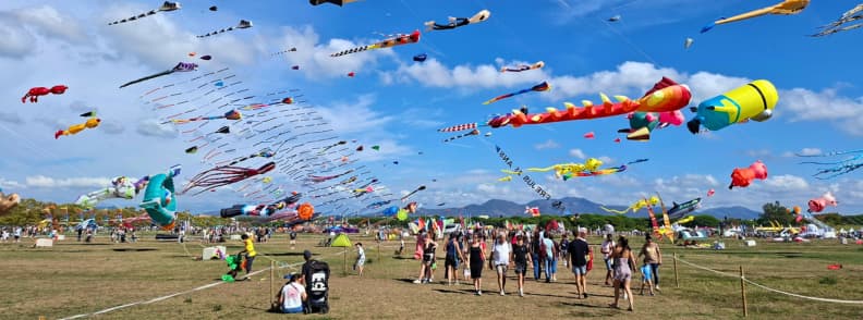 Frejus Kite Festival Arrival Time Crowds and Giant Kites Visitors walking between giant kite fields at the Fréjus International Air Festival, with colorful XXL kites filling the sky above Base Nature François Léotard.