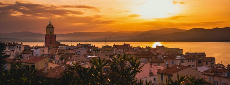 French Riviera Autumn Trip Planning Saint Tropez Sunset Saint-Tropez at sunset in autumn, with the church bell tower, terracotta rooftops, the Gulf of Saint-Tropez, and Maures hills beyond.