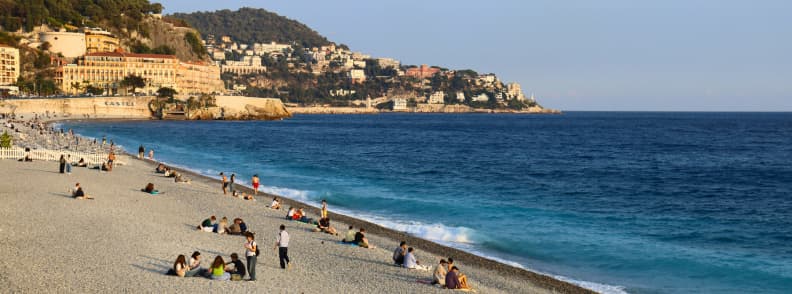 Living Near Frejus Autumn on the French Riviera Autumn on the French Riviera, with people relaxing on a pebble beach beside deep blue Mediterranean water, hillside hotels, and coastal buildings.