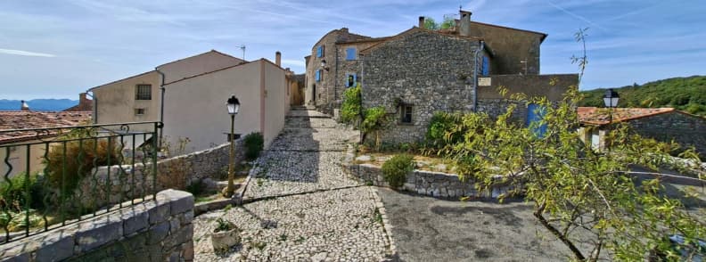 Mons Var FAQ What to Know Before Visiting Stone-paved street climbing through the old village of Mons Var, with traditional houses, blue shutters, and distant Pays de Fayence views.