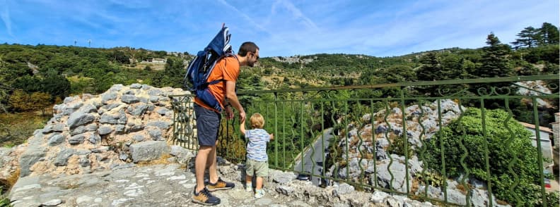 Mons Var Location in Pays de Fayence Provence Father and toddler overlooking the winding mountain road below Mons Var, with rocky slopes and wooded hills surrounding the village.