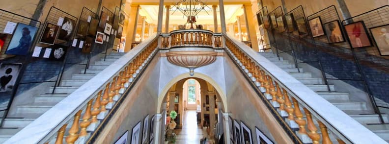 Villa Aurelienne Frejus Grand Double Staircase Interior Grand double staircase inside Villa Aurélienne in Fréjus, with carved balustrades, marble steps, arched passageways, and photographs exhibited during the 2026 surrealist photography festival.