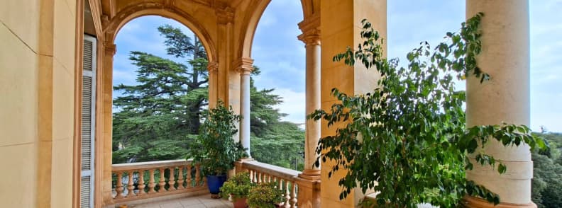 Villa Aurelienne Frejus Palladian Loggia and Park Views Covered loggia at Villa Aurélienne in Fréjus, with tall stone columns, rounded arches, a balustrade, potted plants, and views of the trees in Parc Aurélien.