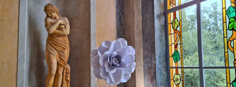 Villa Aurelienne Frejus. Classical female statue beside a giant lavender flower and colorful stained-glass window overlooking trees inside Villa Aurélienne in Fréjus.